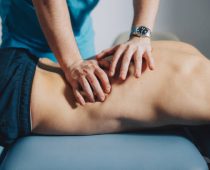 kiné Physical therapist is using his hands to massage the lower back of a male patient lying on his stomach.